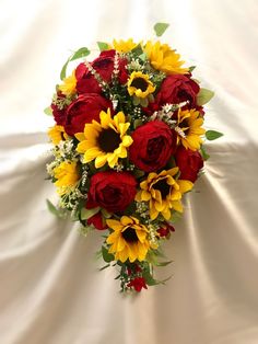 a bouquet of sunflowers and red roses on a white sheet with greenery