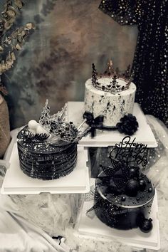 two cakes sitting on top of white trays covered in frosting and black decorations