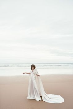 a woman in a white dress standing on the beach with her arms spread wide open