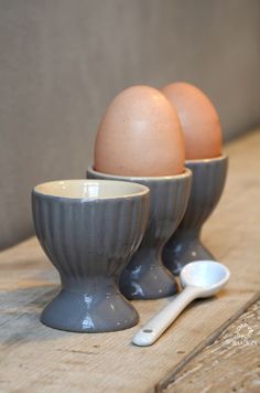 three eggs are in gray bowls with spoons on a wooden countertop next to each other