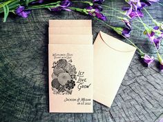 two envelopes sitting next to each other on top of a wooden table with purple flowers