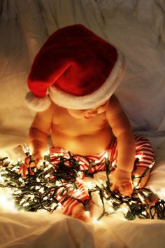 a baby wearing a santa hat sitting on top of a bed next to christmas lights