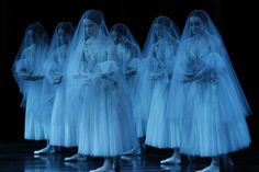 several women in white dresses and veils are standing on a stage with their hands together