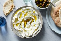 a bowl of hummus, pita bread and olives are on the table