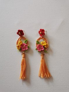 two pairs of earrings with flowers and tassels on them sitting on a white surface