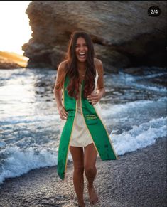 a woman standing on top of a beach next to the ocean wearing a green and yellow coat