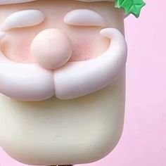 a close up of a plastic santa clause head on a pink background with green leaves