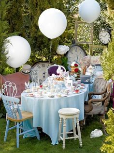 a table set up with balloons, plates and cups on it in the middle of a garden