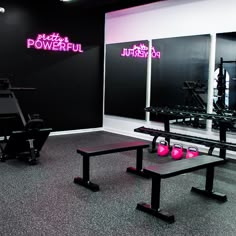 a gym with benches, exercise equipment and pink neon signs on the wall behind them