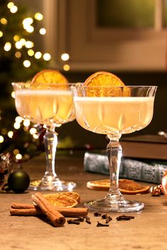 two glasses filled with drinks sitting on top of a table next to a christmas tree