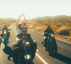 three people on motorcycles riding down the road with their arms in the air and one person waving