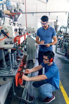 two men working on machinery in a factory with headphones and ear phones around their necks