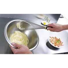 two hands whisk batter into a metal bowl on a stainless steel countertop