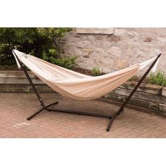 a white hammock sitting on top of a metal stand next to a stone wall