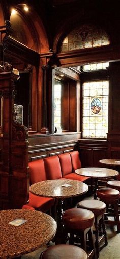 an empty restaurant with wooden tables and stools in front of the counter, along with red upholstered seats