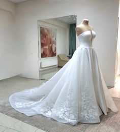 a white wedding dress is on display in a room with a large mirror behind it