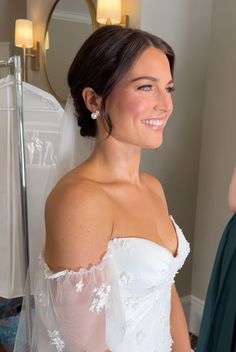 a woman in a wedding dress standing next to a mirror and smiling at the camera