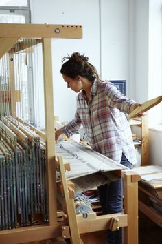 a woman working on a weaving machine in a room with lots of wood and wire