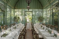 a long table set up with white linens and place settings in a green room