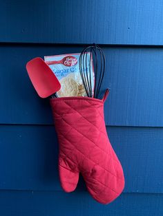 an oven mitt hanging on the side of a blue wall with baking utensils in it