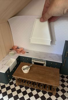 a hand reaching for a piece of furniture in a dollhouse kitchen