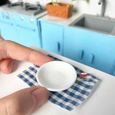 a person is pointing at a small white bowl on a blue and white checkered napkin