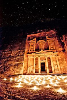 an ancient building lit up at night in front of a rock face with stars above it