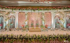 an elaborately decorated banquet hall with flowers and greenery on the walls, couches and tables