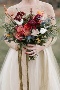 a woman holding a bouquet of flowers in her hands and wearing a dress with sheer sleeves