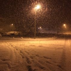 a street light in the middle of a snow storm at night with cars parked along side it