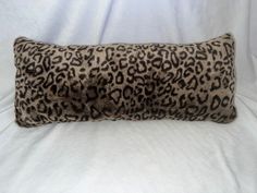 a leopard print pillow on a white bed with a black and brown fur trimming