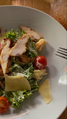 a salad with meat, cheese and tomatoes in a white bowl on a wooden table