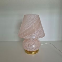 a pink lamp sitting on top of a white table next to a light bulb with a gold base