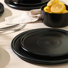 black plates and silverware on a white table cloth with lemons in the background