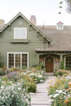 a green house with lots of flowers and plants around the front door is surrounded by greenery