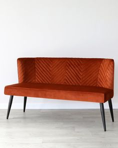 an orange velvet couch with black legs on a wooden floor in front of a white wall