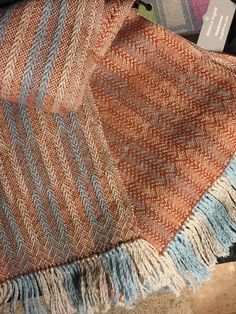 an orange, blue and white blanket sitting on top of a wooden floor next to a pile of books