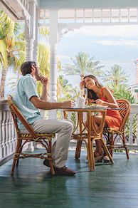 a man and woman sitting at an outdoor table on the porch talking to each other