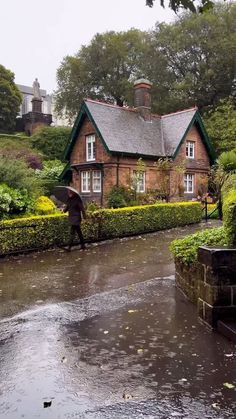 a person with an umbrella walking down a rain soaked street in front of a house