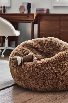 a brown dog bed sitting on top of a wooden floor next to a white chair