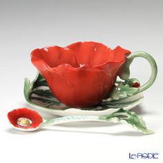 a red flower sitting on top of a green cup and saucer next to a spoon