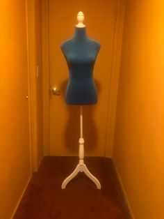 a blue mannequin sitting on top of a white stand next to a door