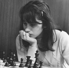 a woman sitting at a chess table with her hand on her chin and looking down