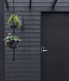 two hanging planters on the side of a black building with a door and window