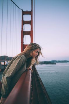 a woman standing on the side of a bridge with her hair blowing in the wind