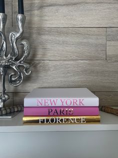 three books are stacked on top of each other in front of a candle holder and wallpaper