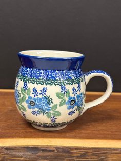 a blue and white flowered mug sitting on top of a wooden table next to a black wall