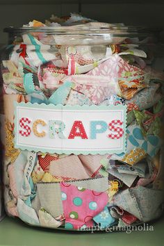 a glass jar filled with lots of different types of fabric and scraps on top of a green shelf