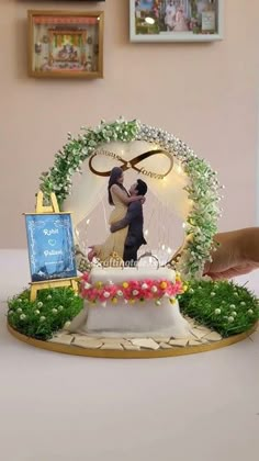 a cake with a couple on it and flowers around the top, surrounded by greenery