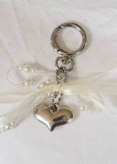 a heart shaped keychain with pearls and a ribbon around it on a white background